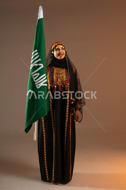 رفع علم التأسيس بإيماءات الثقة و الفخر بانجازات الوطن، الأزياء الشعبية التقليدية، بورتريه لامرأة عربية خليجية سعودية ترتدي زي المنطقة الوسطى، ذكرى تسيس الدولة السعودية الأولى ٢٢ فبراير،  مفهوم حب الوطن و الارتباط  به، يوم بدينا١٧٢٧م، صورة لكامل الجسم