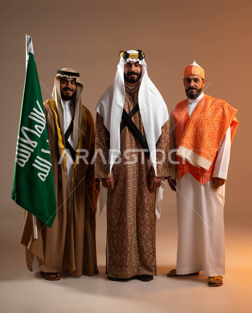 الوقوف بجانب علم التأسيس بثقة وفخر, توارث حب الوطن من الأجداد, بورتريه لمجموعة رجال عرب خليجين سعوديين يرتدون الأزياء الشعبية التقليدية في المناسبات الوطنية, يوم بدينا 1727م, ذكرى تأسيس الدولة السعودية الأولى في 22 فبراير, صورة الجسم بالطول الكامل, خلفية بيج
