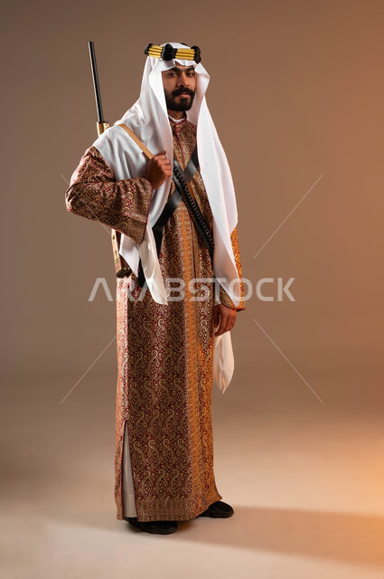 إظهار مشاعر التباهي والفخر بإنجازات البلاد, بورتريه لشاب عربي خليجي سعودي يرتدي أزياء المنطقة الوسطى في المناسبات الوطنية يمسك بيده البندقية, يوم بدينا 1727م, ذكرى تأسيس الدولة السعودية الأولى في 22 فبراير, صورة الجسم بالكامل, خلفية بيج