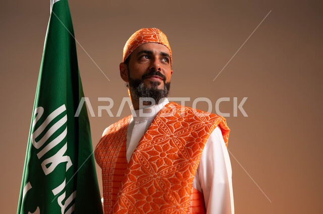 Anniversary of the founding of the first Saudi state on February 22, raising the founding flag with love and pride in the nation’s achievements, close-up portrait of a Saudi Gulf Arab man wearing the popular Sudairi and traditional thobe looking at something, Day of Our Day 1727 AD, wearing the costumes of the Western Region on national occasions, beige background