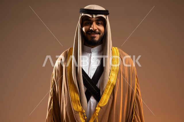 ذكرى تأسيس الدولة السعودية الأولى في 22 فبراير, يوم بدينا 1727م, الوقوف بثقة بإنجازات البلاد, إظهار مشاعر الولاء للوطن, بورتريه مقرب لشاب عربي خليجي سعودي يرتدي الجبة والمحزم والعقال ينظر إلى الكاميرا, ارتداء الأزياء الشعبية في المناسبات الوطنية، خلفية بيج