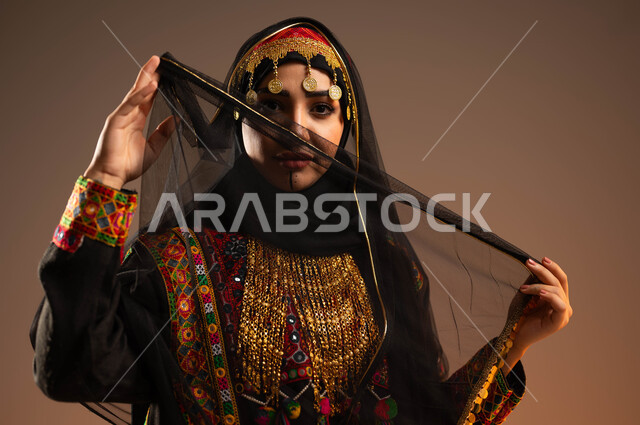 Softness, gentleness and highlighting the beauty of the Gulf, a close-up portrait of a Saudi Gulf Arab young woman wearing a muqata, shayla and hama looking at the camera, Day of Our Day 1727 AD, anniversary of the founding of the first Saudi state on February 22, wearing traditional folk costumes on national occasions, beige background