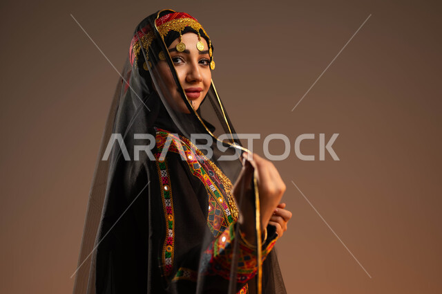 الوقوف بثقة وفخر بالانتماء للوطن, بورتريه مقرب من الجانب لشابة عربية خليجية سعودية ترتدي الشيلة والمقطع والهامة تنظر إلى الكاميرا, يوم بدينا 1727م, ذكرى تأسيس الدولة السعودية الأولى في 22 فبراير, ارتداء أزياء المنطقة الوسطى في المناسبات الوطنية, خلفية بيج