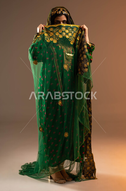 الفخر بالانتماء السعودي, النعومة وإبراز الجمال الخليجي, يوم بدينا 1727م, بورتريه لشابة عربية خليجية سعودية ترتدي الهامة والبشت تنظر إلى الكاميرا, ذكرى تأسيس الدولة السعودية الأولى في 22 فبراير, إظهار الحب والولاء للدولة, صورة الجسم بالطول الكامل, خلفية بيج