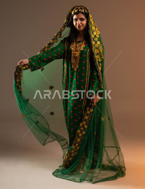 ذكرى تأسيس الدولة السعودية الأولى في 22 فبراير, ارتداء أزياء المنطقة الوسطى في المناسبات الوطنية, الفخر والتباهي بإنجازات البلاد, بورتريه لشابة عربية خليجية سعودية ترتدي المقطع والهامة والبشت تنظر إلى الكاميرا, يوم بدينا 1727م, صورة الجسم بالكامل, خلفية بيج