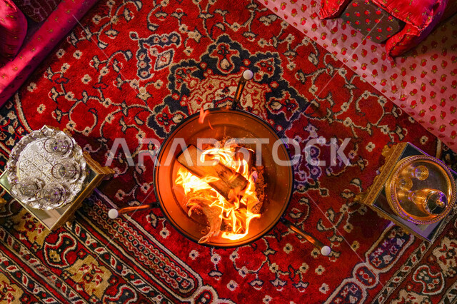 صورة علوية علمودية مجلس عربي شعبي فاخر، العادات والتقاليد السعودية في تقديم القهوة العربية بالدله والفنجان، التدفئة على موقد الحطب في الأجواء الشتوية، جلسات شعبية تلقيدية