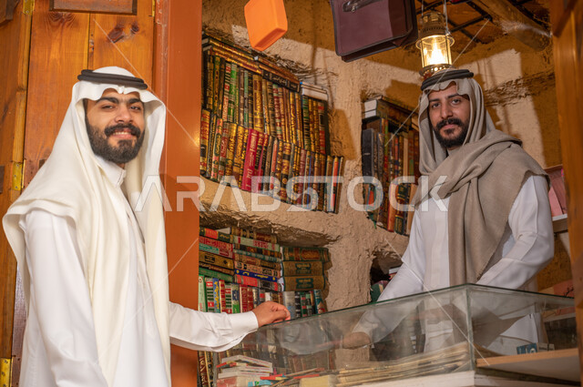 استعارة الكتب من المكاتب التاريخيه المبنية على الطراز القديم، دعم وتنمية الذخيرة اللغوية والعلمية, شاب عربي خليجي سعودي يرتدي الزي التقليدي يقوم باقتناء كتاب من المكتبة, ذكرى تأسيس الدولة السعودية الأولى 22 فبراير، يوم بدينا 1727 م