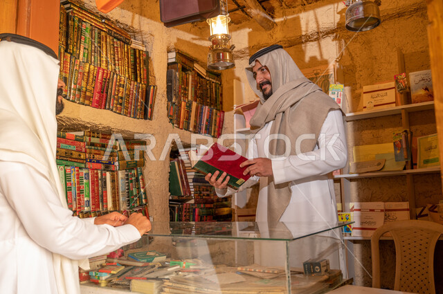 استعارة الكتب من المكاتب التاريخيه المبنية على الطراز القديم، دعم وتنمية الذخيرة اللغوية والعلمية, شاب عربي خليجي سعودي يرتدي الزي التقليدي يقوم باقتناء كتاب من المكتبة, ذكرى تأسيس الدولة السعودية الأولى 22 فبراير، يوم بدينا 1727 م