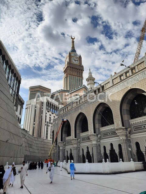 التجمع الاسلامي من كل انحاء العالم لأداء العبادات والتقرب الى الله, الفنادق والأبراج الفاخرة المحيطة بالمسجد, الحجاج والمعتمرين في الساحة الخارجية للحرم المكي في مكة المكرمه، أماكن ومعالم دينية اسلامية مقدسة, السماء الزرقاء المليئة بالغيوم