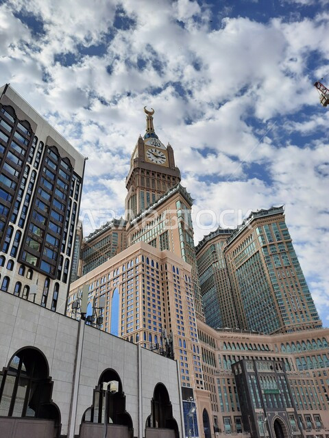The clock tower overlooking the Holy Mosque in Mecca, the development of architectural engineering for the luxury hotels and towers surrounding the Grand Mosque, sacred Islamic religious places and landmarks, a view of the blue sky filled with clouds