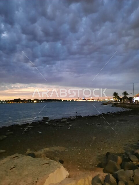 الواجهة البحرية المضاءة في وقت الليل، معالم سياحيه ترفيهية مشهورة في المملكة العربية السعودية، الاستمتاع بمنظر البحر في شاطئ جدة السياحي, أماكن الرحلات والنزهات العائلية في العطلة الصيفية، السماء الملبدة بالغيوم