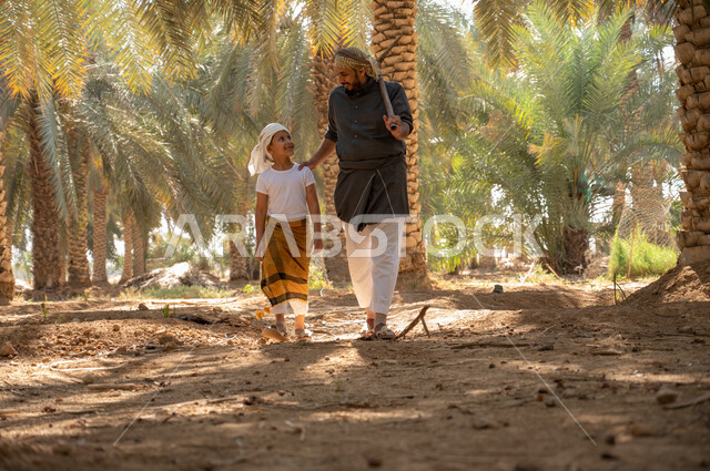 الاهتمام في زراعه اشجار النخل، الحفاظ على تراث زراعي غني ،الاستعداد لحراثة الارض الزراعيه، فلاح عربي خليجي سعودي يرتدي الزي الشعبي التقليدي يحمل بيده أداة الحفر يتجول مع ابنه داخل مزارع النخيل المثمرة بإيماءات السرور، محاصيل زراعيه محليه
