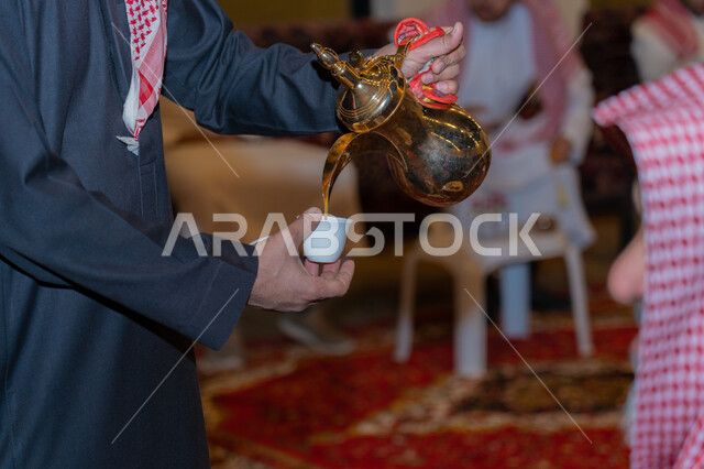 مفهوم حسن الاستقبال وكرم الضيافة، تقديم المشروبات الساخنة في المناسبات والأعياد، توارث العادات والتقاليد، صورة مقربة لرجل عربي خليجي سعودي يرتدي الزي التقليدي يقوم بصب القهوة من الدلة النحاسية 