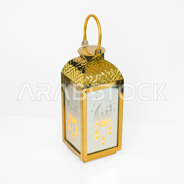 فوانيس وتحف اسلامية تقليدية للاحتفال بقدوم شهر الخير، أنوار ومصابيح في الأجواء الرمضانية الروحانية، إضاءة وزينة شهر رمضان المبارك، فانوس عربي معدني مزخرف باللون الذهبي، خلفية بيضاء