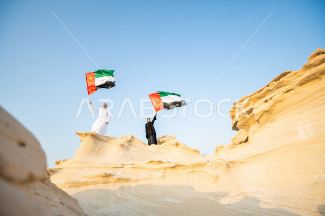 زوجان اماراتيان  يحتفلان باليوم الوطني لدولة الامارات العربية المتحدة ، يحملان علم دولة الامارات في احدى المناطق الصحراوية بالامارات ، ذكرى اليوم الوطني الاماراتي ، يوم الاستقلال ، الوطني الاماراتي
