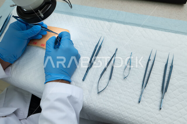الخبرة و المهارة في التطبيب، صورة مقربة ليدي طبيب يرتدي القفازات الطبية يقوم بالتدريب على خياطة الجروح، أدوات جراحية من الفولاذ المقاوم للصدأ