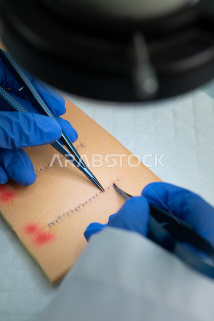 Close-up of a doctor's hands wearing medical gloves practicing wound suturing, stainless steel surgical instruments, experience and skill in medicine.
