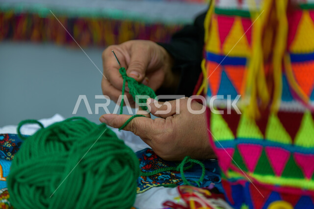 Ancient women's professions and crafts, handicrafts and crafts, popular traditional works, the art and skill of sewing and spinning, a close-up of the hand of a Saudi Gulf Arab woman knitting wool, using colored woolen threads, pride and flaunting of the Saudi Gulf heritage