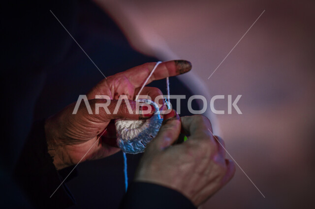  أعمال تقليدية شعبية, مشغولات وصناعات يدوية, فن ومهارة الخياطة والغزل, صورة مقربة ليد إمرأة عربية خليجية سعودية تقوم بحياكة الصوف, استخدام خيوط صوفية ملونة, الفخر والتباهي التراث الخليجي السعودي, مهن وحرف نسائية
