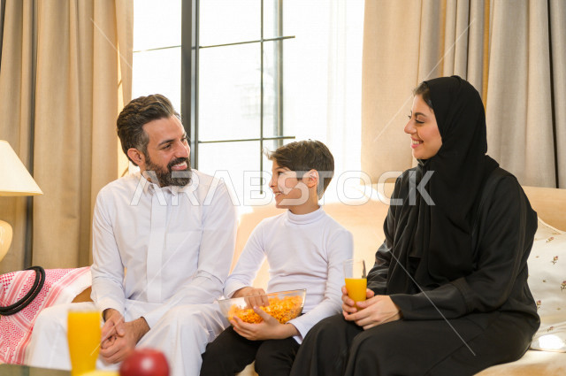 أسرة خليجية صغيرة وسعيدة تجلس على الأريكة في المنزل ، الاستمتاع بقضاء الوقت مع العائلة ، يوم الطفل العالمي ، عائلة سعودية ، اجواء عائلية سعيدة 