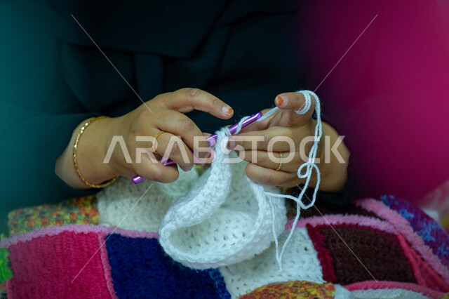 مشغولات وصناعات يدوية, أعمال تقليدية شعبية, فن ومهارة الخياطة والغزل, صورة مقربة ليد إمرأة عربية خليجية سعودية تقوم بحياكة الصوف, استخدام خيوط صوفية بيضاء, الفخر والتباهي بالحرف والتراث الخليجي السعودي