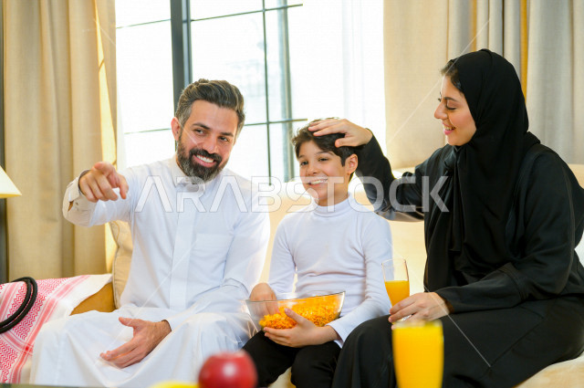 أسرة خليجية صغيرة وسعيدة تجلس على الأريكة في المنزل ، الاستمتاع بقضاء الوقت مع العائلة ، يوم الطفل العالمي ، عائلة سعودية ، اجواء عائلية سعيدة 
