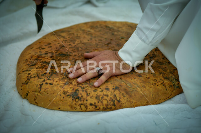 منتجات محلية وطنية, مهارة صنع المخبوزات, مأكولات ومعجنات شرقية طازجة, صورة مقربة ليد رجل عربي خليجي سعودي يقوم بتقطيع قطعة الكعك, مهن تقليدية شعبية, فطور صباحي شهي