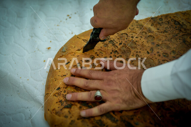 منتجات محلية وطنية, مهارة صنع المخبوزات, مأكولات ومعجنات شرقية طازجة, صورة مقربة ليد رجل عربي خليجي سعودي يقوم بتقطيع قطعة الكعك, مهن تقليدية شعبية, فطور صباحي شهي