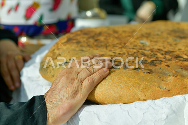 فطور صباحي شهي, منتجات محلية وطنية, مهارة صنع المخبوزات, مأكولات ومعجنات شرقية طازجة, صورة مقربة ليد إمرأة عربية خليجية سعودية تمسك بيدها قطعة الكعك, مهن تقليدية شعبية