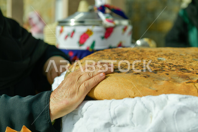 فطور صباحي شهي, منتجات محلية وطنية, مهارة صنع المخبوزات, مأكولات ومعجنات شرقية طازجة, صورة مقربة ليد إمرأة عربية خليجية سعودية تمسك بيدها قطعة الكعك, مهن تقليدية شعبية