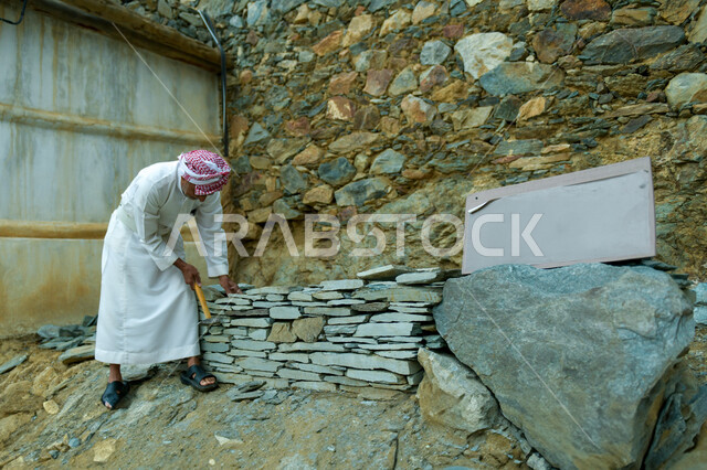 إعادة بناء وترميم البيوت والمنشآت القديمة, مفهوم التمسك بالأصالة والتراث السعودي, رجل كبير بالسن عربي خليجي سعودي يرتدي الثوب التقليدي والشماغ يمسك بيده الحجارة, الآثار والأماكن التاريخية الشعبية