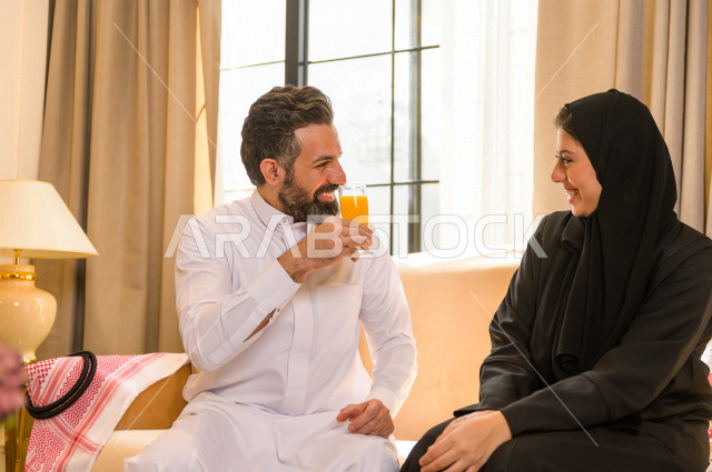 زوجان خليجيان سعيدان يجلسان على الأريكة في المنزل ، الاستمتاع بقضاء الوقت في المنزل ، قضاء وقت الفراغ مع العائلة ، اسره سعودية خليجية