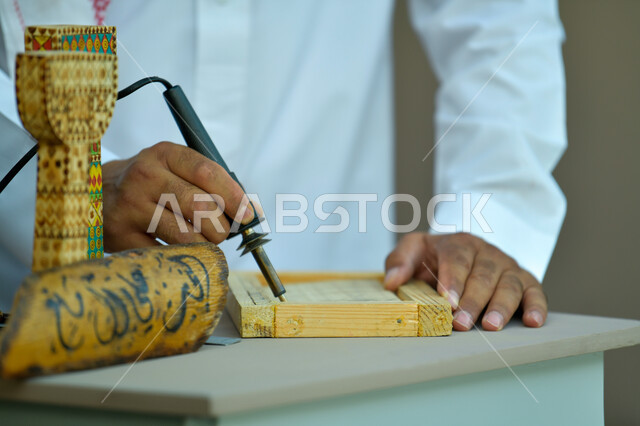 الأصالة والعراقة والفخر و الاعتزاز بالتراث السعودي، الرسم والتخطيط اليدوي، صورة مقربة لأيدي رجل عربي خليجي سعودي يقوم بالنقش على قطع خشبية ،مهن وحرف شعبيه تراثية، تحف أثرية تقليدية