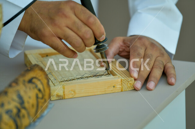 الرسم والتخطيط اليدوي، صورة مقربة لأيدي رجل عربي خليجي سعودي يقوم بالنقش على قطع خشبية ،مهن وحرف شعبيه تراثية،  الأصالة والعراقة والفخر و الاعتزاز بالتراث السعودي، تحف أثرية تقليدية