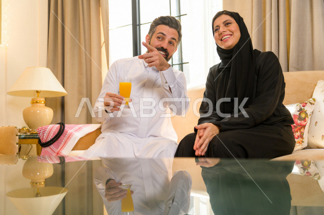 زوجان خليجيان سعيدان يجلسان على الأريكة في المنزل ، الاستمتاع بقضاء الوقت في المنزل ، قضاء وقت الفراغ مع العائلة ، اسره سعودية خليجية