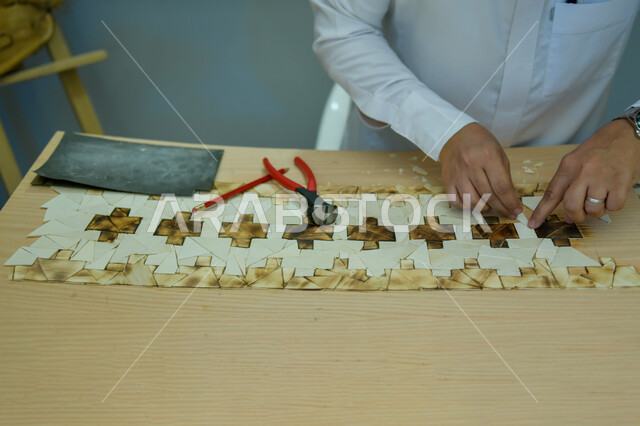 ألعاب الذكاء و التركيز ،مفهوم حل اللغز و التسلية والترفيه، صورة مقربة لأيدي رجل عربي خليجي سعودي يقف في أحد المحلات التجارية ويقوم بقص قطع البازل، أعمال تراثية شعبية، مهن ووظائف سعودية