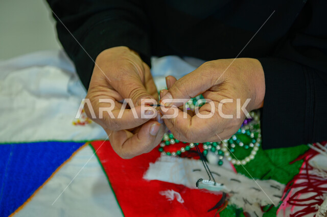  مهن وحرف نسائية قديمة ،مشغولات وصناعات يدوية, أعمال تقليدية شعبية, الفخر والتباهي بالحرف والتراث الخليجي السعودي, صورة مقربة لأيدي امرأة عربيه خليجية سعودية تقوم بضم حبات الخرز لصنع السبحات الاسلامية