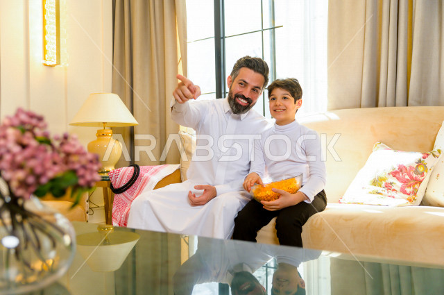 أسرة خليجية صغيرة وسعيدة تجلس على الأريكة في المنزل ، الاستمتاع بقضاء الوقت مع العائلة ، يوم الطفل العالمي ، عائلة سعودية ، اجواء عائلية سعيدة 