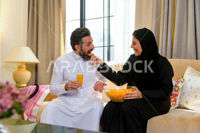 زوجان خليجيان سعيدان يجلسان على الأريكة في المنزل ، الاستمتاع بقضاء الوقت في المنزل ، قضاء وقت الفراغ مع العائلة ، اسره سعودية خليجية