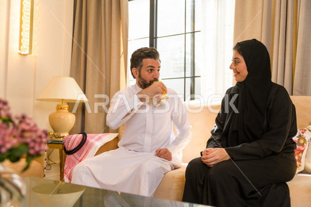 زوجان خليجيان سعيدان يجلسان على الأريكة في المنزل ، الاستمتاع بقضاء الوقت في المنزل ، قضاء وقت الفراغ مع العائلة ، اسره سعودية خليجية