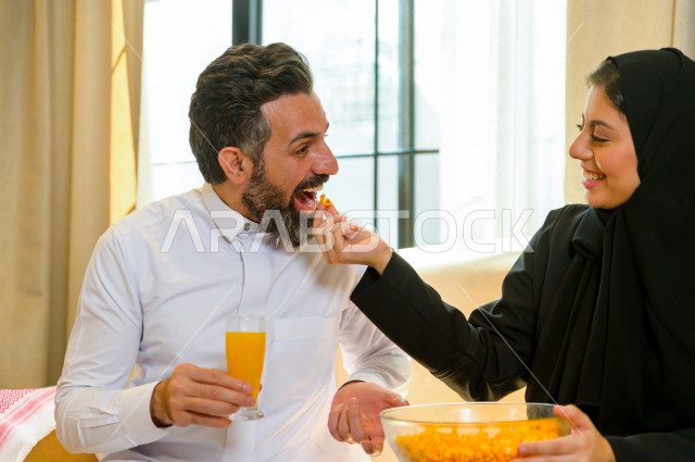 زوجان خليجيان سعيدان يجلسان على الأريكة في المنزل ، الاستمتاع بقضاء الوقت في المنزل ، قضاء وقت الفراغ مع العائلة ، اسره سعودية خليجية