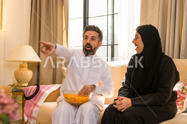 زوجان خليجيان سعيدان يجلسان على الأريكة في المنزل ، الاستمتاع بقضاء الوقت في المنزل ، قضاء وقت الفراغ مع العائلة ، اسره سعودية خليجية