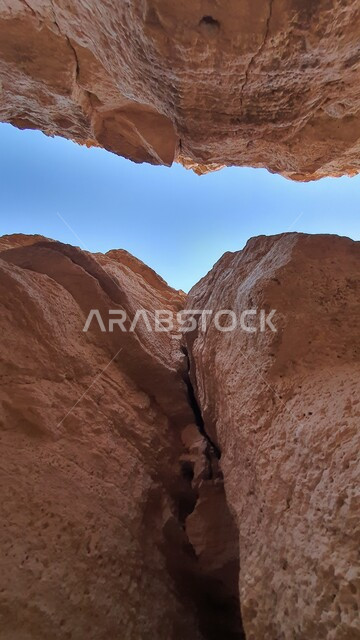 السماء الصافية بين سلسلة جبلية في كهف البرمة داخل صحراء منطقة الثمامة في الرياض، السياحة في السعودية بالمناطق الصحراوية الطبيعية، المرتفعات الصخرية والمعالم الأثرية القديمة في المملكة العربية السعودية