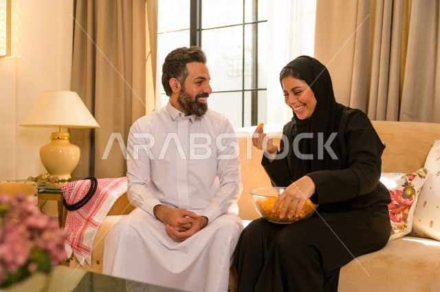 زوجان خليجيان سعيدان يجلسان على الأريكة في المنزل ، الاستمتاع بقضاء الوقت في المنزل ، قضاء وقت الفراغ مع العائلة ، اسره سعودية خليجية