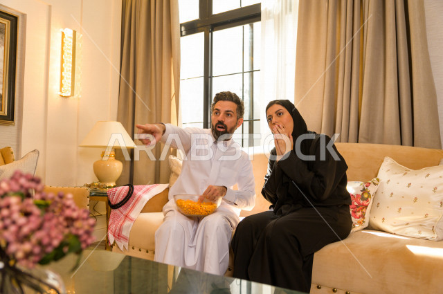 زوجان خليجيان سعيدان يجلسان على الأريكة في المنزل ، الاستمتاع بقضاء الوقت في المنزل ، قضاء وقت الفراغ مع العائلة ، اسره سعودية خليجية