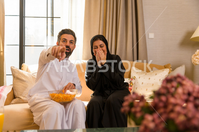 زوجان خليجيان سعيدان يجلسان على الأريكة في المنزل ، الاستمتاع بقضاء الوقت في المنزل ، قضاء وقت الفراغ مع العائلة ، اسره سعودية خليجية