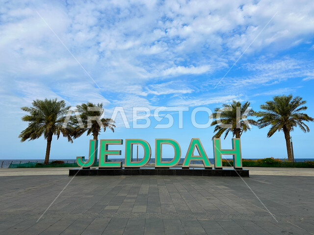 The waterfront on the coast of the Arabian Gulf, a model of the word Jeddah in the English language on the New Jeddah City Corniche, interest in planting green palm trees in coastal cities, famous tourist attractions in the Kingdom of Saudi Arabia.