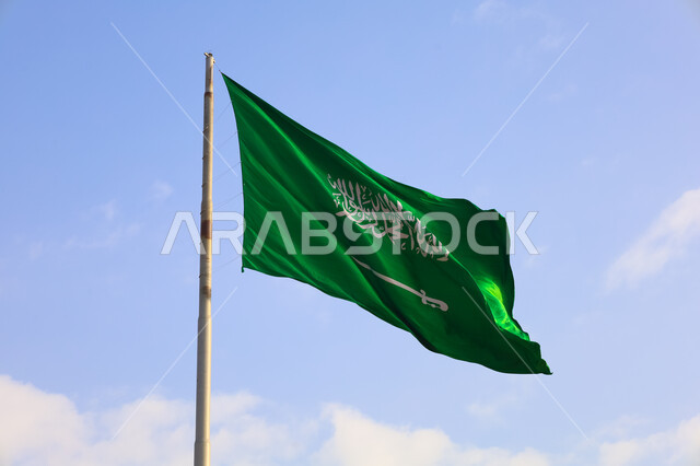 سارية العلم الوطني السعودي يرفرف عاليا وقت النهار، عيد الاستقلال السعودي، الاحتفال بيوم العلم السعودي 11 مارس، صورة مقربة لراية التوحيد و الإسلام مرفوعة في سماء المملكة، الاحتفال بذكرى اليوم الوطني السعودي 23 سبتمبر