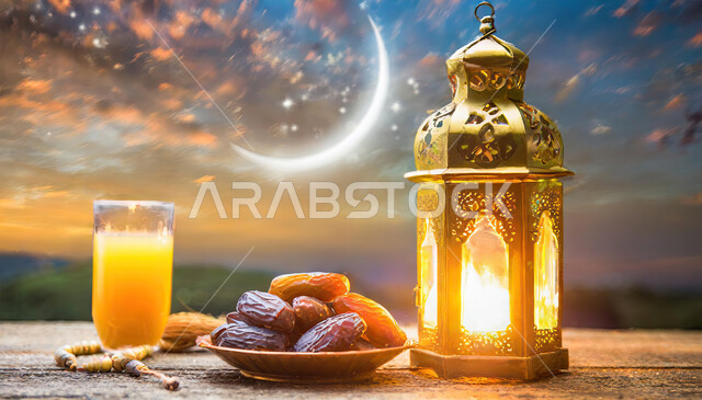 خلفية هلال شهر رمضان في السماء ،فانوس معدني تقليدي مضيء مع كأس من عصير البرتقال الصحي و حبات التمر الطازجة على طاولة خشبية ،أجواء رمضانية روحانية، أعياد ومناسبات دينية ، الاستعداد لاستقبال شهر الخير والبركة