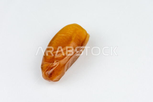 وجبة ذات قيمة غذائية عالية، صورة مقربة لحبة من التمر الصحي شقراء اللون، تمر دقلة نور، ضيافة رمضانية تقليدية، أنواع التمور المتميزة، خلفية بيضاء